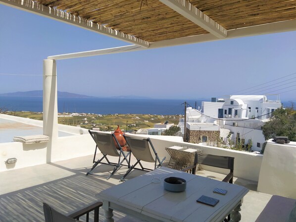 A terrace with a table and chairs, overlooking a coastal town with white buildings and the sea. - Sunny Winehouse. Stylish studio with big terrace and stunning sea - sunset views (Φοινικιά)