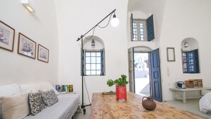 Quarto com mesa de madeira, sofá com almofadas estampadas, quadros nas paredes e uma lata vermelha usada como vaso.