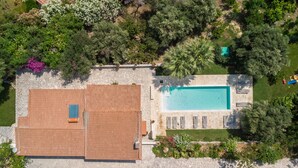 Vue aérienne d’une propriété dotée d’une piscine, d’un patio couvert et d’un jardin agrémenté de diverses plantes et arbres.
