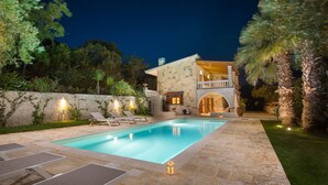 Un espace aménagé au bord de la piscine, avec des chaises longues, une piscine en pierre et un bâtiment en pierre doté d’un balcon.