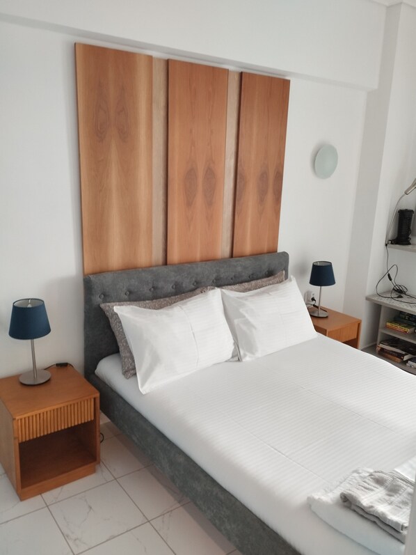 Un dormitorio con una cama, dos mesitas de noche, una lámpara y una estantería con libros.