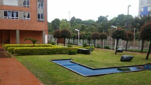 A courtyard with a brick building, neatly trimmed hedges, and a small water feature.
