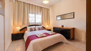 A hotel room with a large bed, two bedside tables with lamps, a wooden desk, and a large window with curtains. - Two bedroom apartment only 500 meters to the beach (Ιαλυσός)