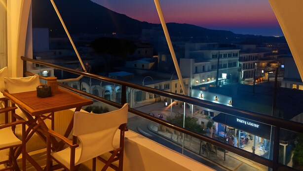 A balcony with a table and chairs, overlooking a cityscape at dusk with buildings and a mountain in the background. - Two bedroom apartment only 500 meters to the beach (Ιαλυσός)