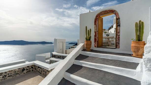 Un edificio blanco con base de piedra, una puerta de madera y vista al mar.