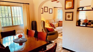 A dining area with a wooden table and chairs, a glass of wine, and a vase of flowers. There is a sofa and a lamp in the background. - Private Villa With Pool Near Golf Course Short Drive to Beach (Unknown)