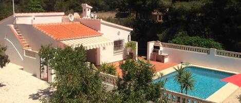 A residential property with a swimming pool, a covered patio, and a view of a hilly landscape.