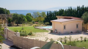 Ein kleines Haus mit Pool, umgeben von viel Grün und Blick auf das Meer.