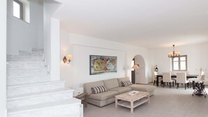 Een ruime woonkamer met een trap, een beige bank, een eettafel met stoelen en een kroonluchter.