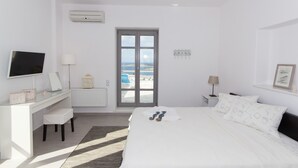 Een hotelkamer met een bed, een bureau, een televisie en uitzicht op de zee door een deur.