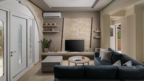 Un saló modern amb una paret de pedra, un televisor de pantalla plana, un sofà blau fosc i una taula de centre petita i rodona.