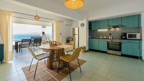Una cocina moderna con gabinetes azul turquesa, un horno de acero inoxidable y un microondas. Hay una zona de comedor con una mesa redonda y sillas de mimbre.