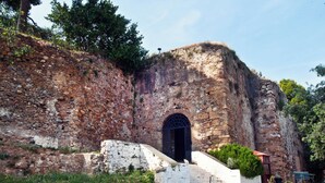 Una estructura de piedra antigua con una gran entrada arqueada, una escalera que lleva a ella y un pequeño banco cerca.