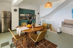 Eine moderne Küche mit türkisgrünen Schränken, einem Edelstahl-Kühlschrank und einer Essecke mit Holztisch und Korbstühlen.