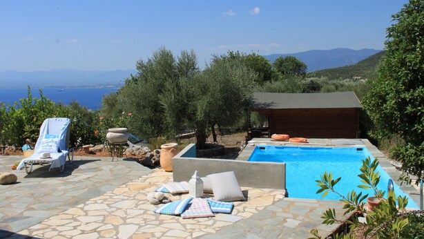 Zona de piscina con vista al mar, suelo de piedra y una tumbona.
