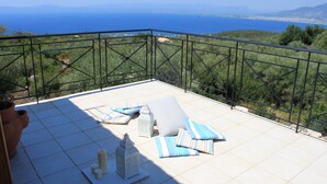 Una terraza con vistas al mar, con barandilla, piso de baldosas y cojines de exterior.