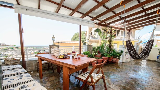 A covered patio with a wooden table, cushioned seating, and potted plants. - Arch Villa traditional holiday house on Rhodes (Σορωνή)