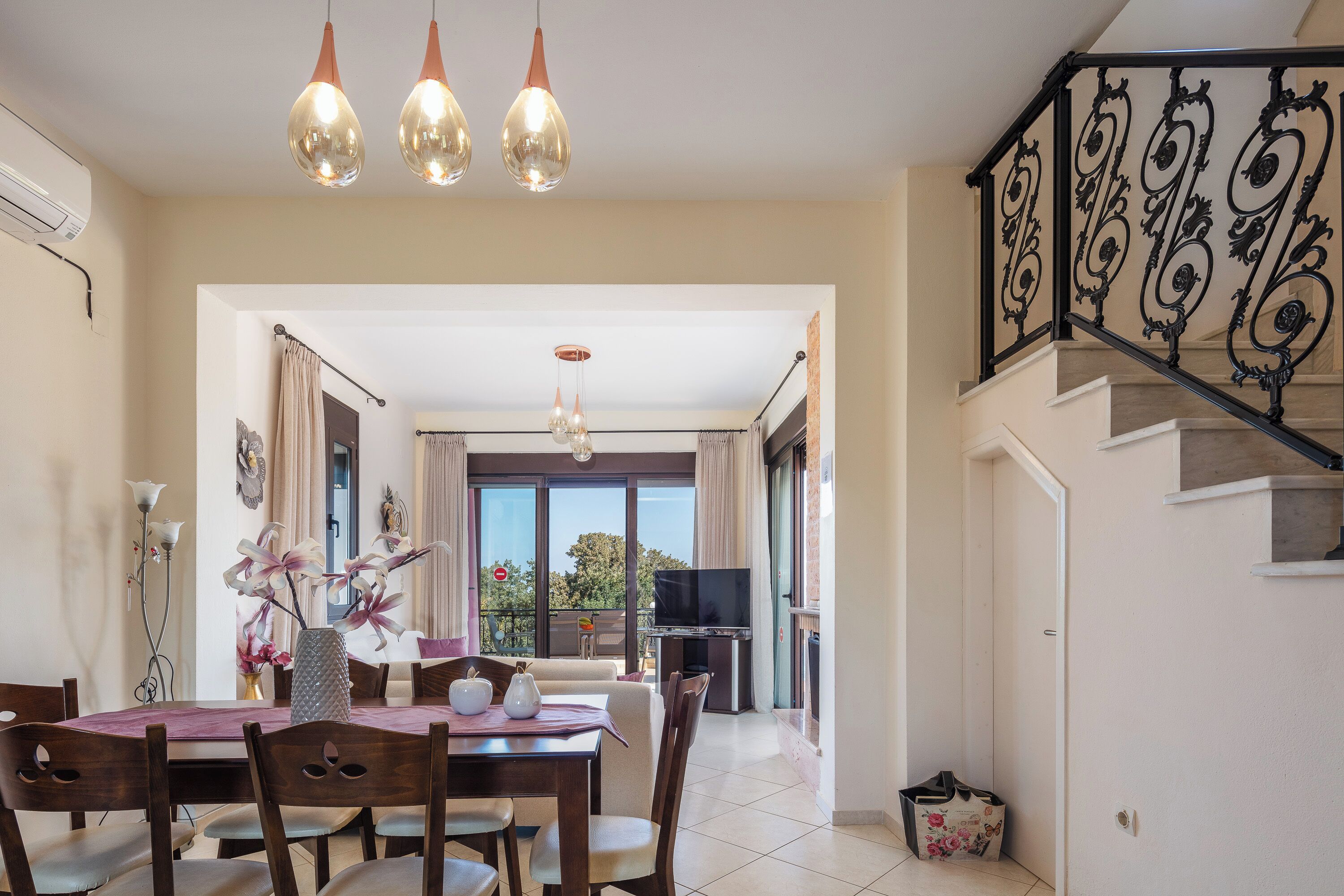 A dining area with a table set for four, a chandelier, and a view to a balcony.