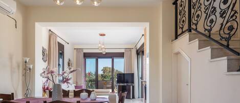A dining area with a table set for four, a chandelier, and a view to a balcony.