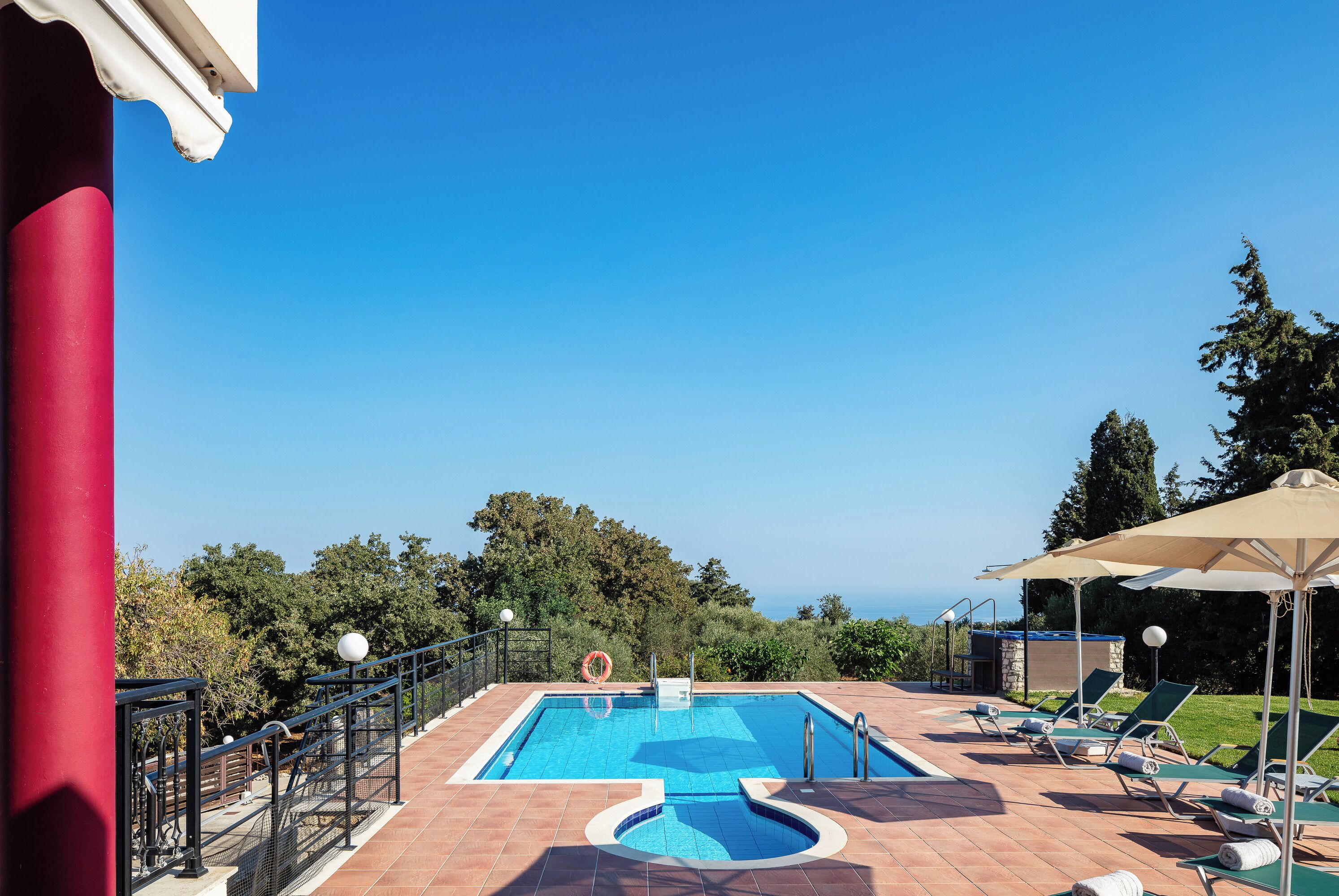 Ein Poolbereich mit Meerblick, umgeben von Gr ünflächen und ausgestattet mit Liegestühlen und Sonnenschirmen.