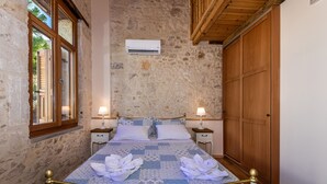 A bedroom with a stone wall, wooden ceiling, a bed with a blue and white quilt, two bedside tables with lamps, and a wooden wardrobe.