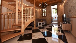 A spacious room with a wooden staircase, a checkered floor, a sofa, a small table, and a television.