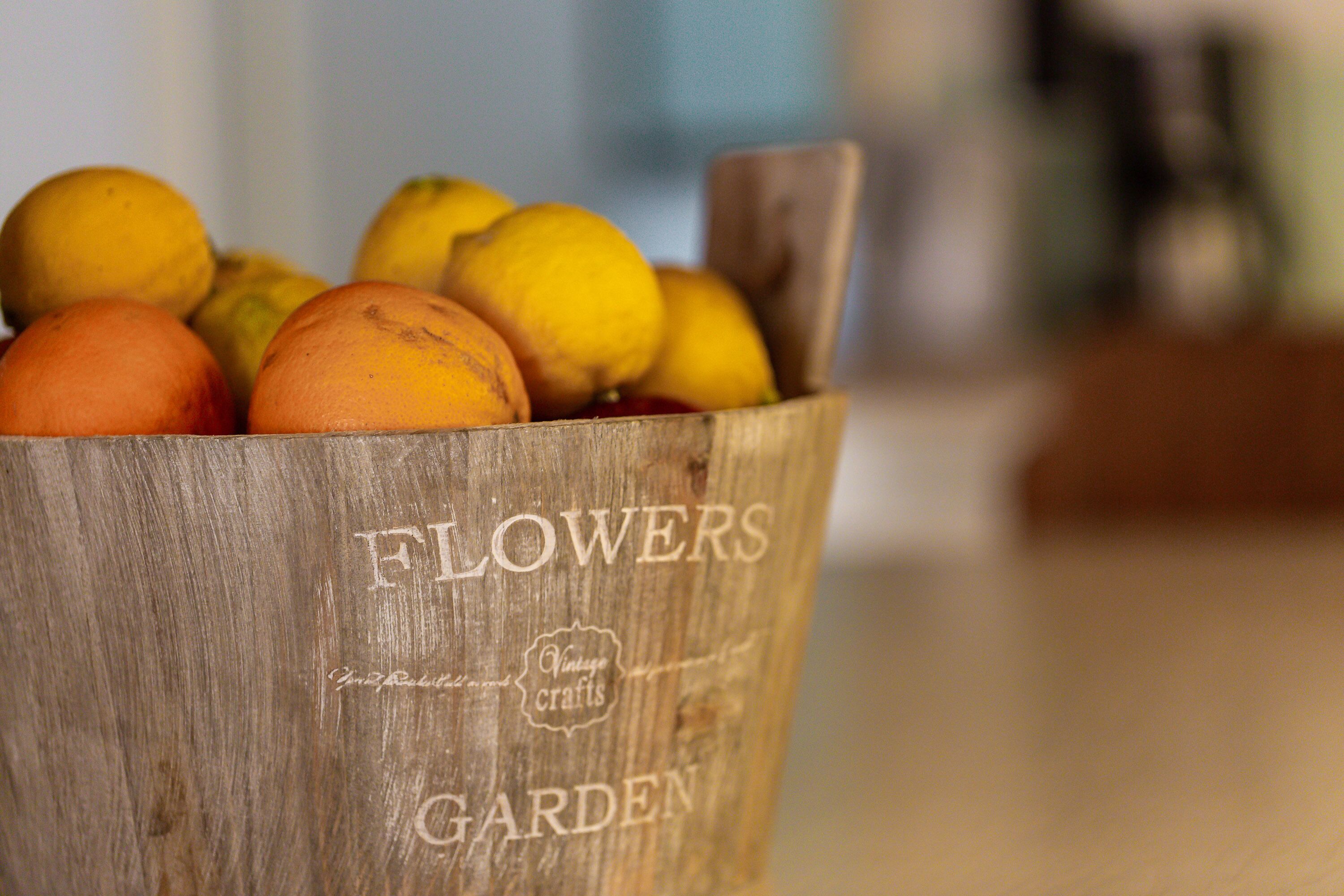 Un seau en bois portant l’inscription « JARDIN DE FLEURS » et rempli d’oranges et de citrons.