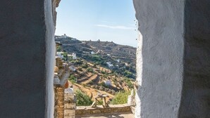 A stone staircase leading to a balcony overlooking a village with traditional buildings and a clear sky. - "Art House"          (Τήνος)