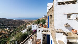 A white building with a blue door, terracotta pots, and a view of the sea. - "Art House"          (Τήνος)