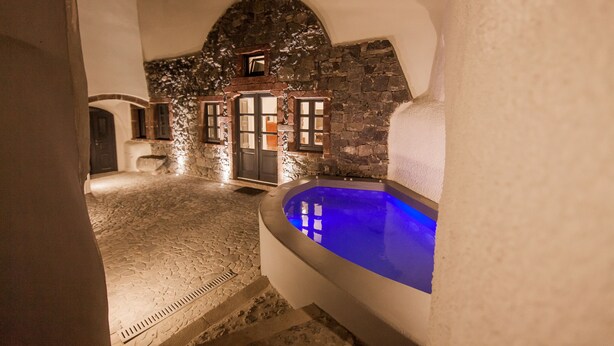 Ein Wellnessbereich mit Steinböden, einer blau beleuchteten Whirlwanne, Steinwänden und einer Tür zu einem Raum.