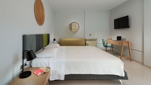 A hotel room with a bed, bedside table, lamp, and a desk with a chair. - Apartment very close to the water and the beach (Χανιά)