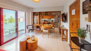 A modern kitchen with wooden cabinets, a dining area with a round table, and a sliding glass door leading to an outdoor patio. - Apartment very close to the water and the beach (Χανιά)