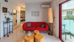 A modern living room with a red sofa, wooden coffee table, and a large window with a view of the outside. - Apartment very close to the water and the beach (Χανιά)