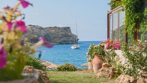 A coastal view with a sailboat, rocky cliffs, and potted plants.