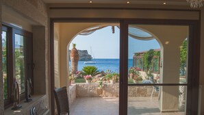 A room with a view of the sea, a balcony with potted plants, and a chair.