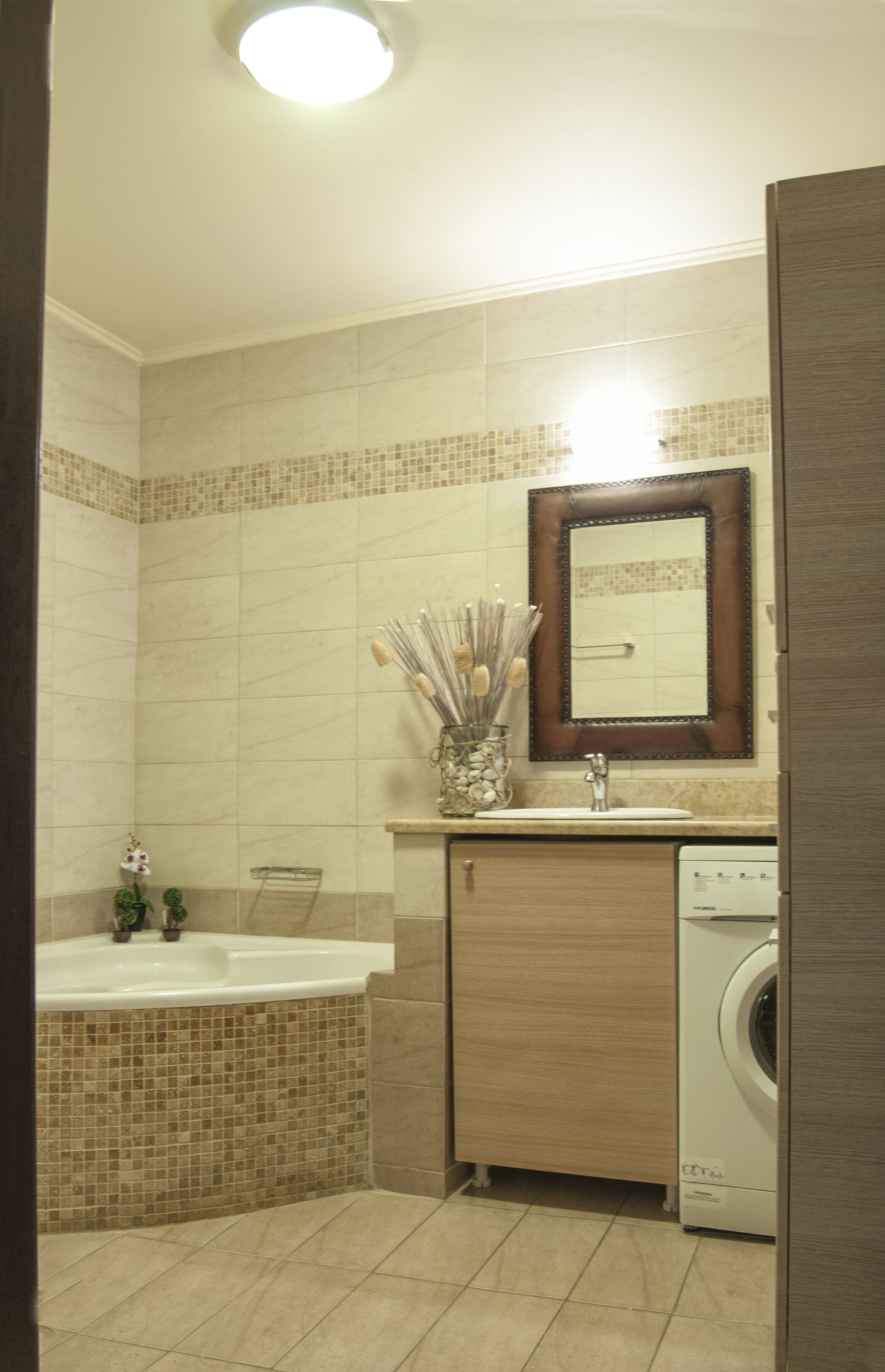 Un baño con suelo de baldosas, un lavabo, un espejo, toallero, ducha y lavadora.