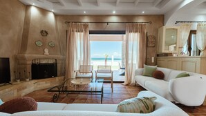 Un salón espacioso con chimenea, sofás blancos y vistas al mar a través de amplias ventanas.