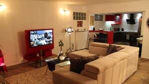 Una sala de estar con un sofá color beige, un mueble para televisor rojo y una mesa de centro de vidrio.