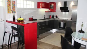 Una cocina moderna con armarios rojos, una isla central, sillas negras y una pequeña mesa de comedor.