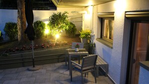 Un patio al aire libre con una mesa, sillas, una planta en maceta y un árbol.