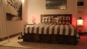 Un dormitorio con una cama grande, cabecera, mesita de noche con lámpara y un espejo adosado a la pared.