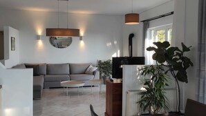 Un salon moderne avec un canapé gris, deux petites tables rondes, une table à manger avec des chaises et une grande plante en pot.