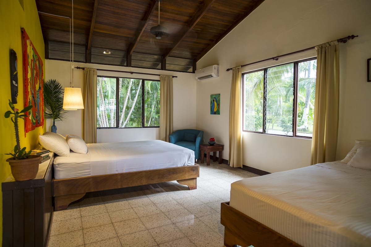 A room with two beds, a chair, a small table, and a potted plant.