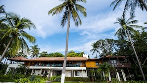 A two-story building with a balcony, surrounded by palm trees and lush greenery. - Playa Junquillal Eco Resort (Santa Cruz)