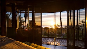 A room with a bed, a balcony with a view of the sunset, and a railing. - Playa Junquillal Eco Resort (Santa Cruz)