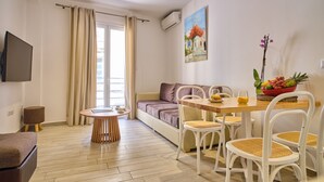 Een moderne woonkamer met een bank, een eettafel met stoelen, een aan de muur bevestigde televisie en een raam met gordijnen.