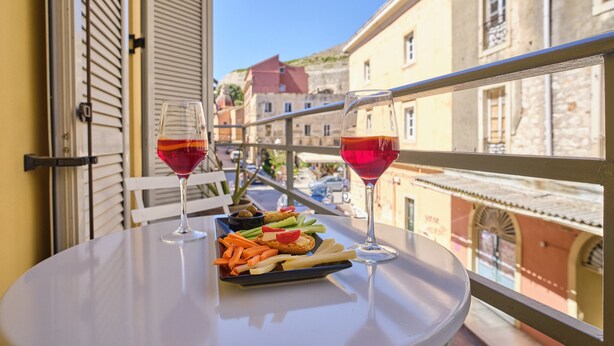 Een balkon met een gedekte tafel, inclusief een bord eten en twee glazen rode wijn.