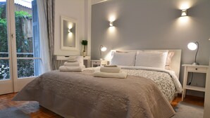 Una camera da letto con un letto grande, due comodini, un tavolino e una finestra con tende, affacciata su una vista verde.