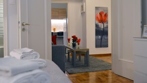 Una camera d'hotel con un letto, un tavolino con un vaso di fiori, un quadro al muro e vista sulla stanza confinante.