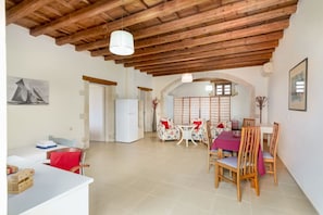 Un'ampia stanza con soffitto in legno, zona pranzo con tavolo e sedie, divano e frigorifero.